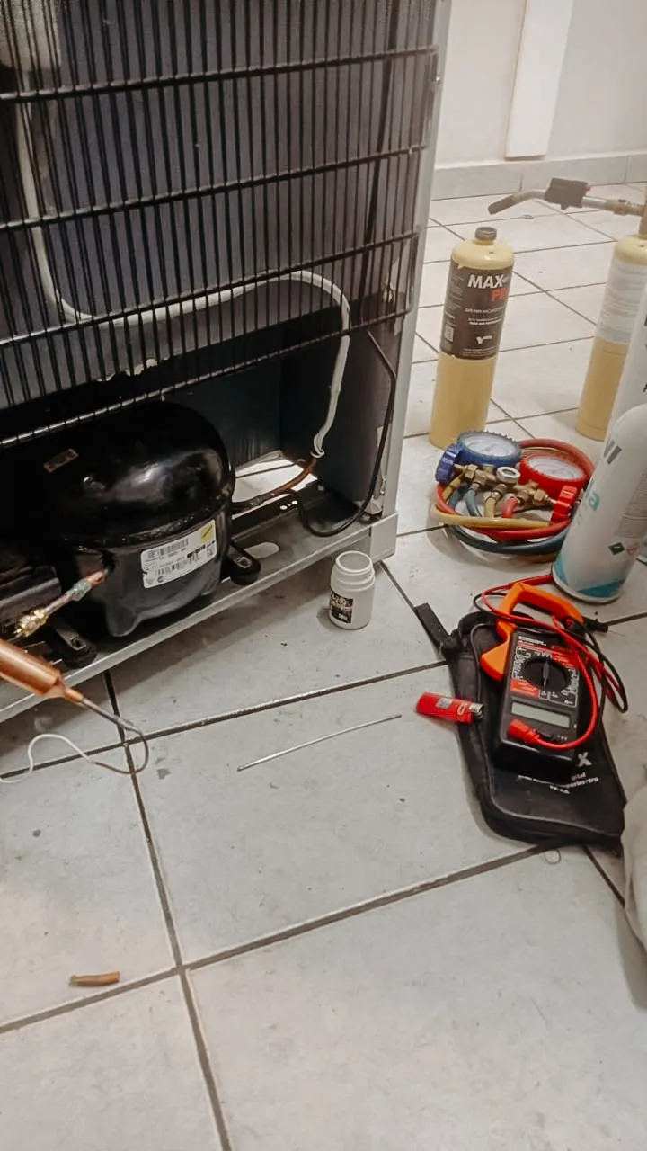 Compressor de geladeira em conserto, com manômetro, multímetro e cilindros de gás ao lado